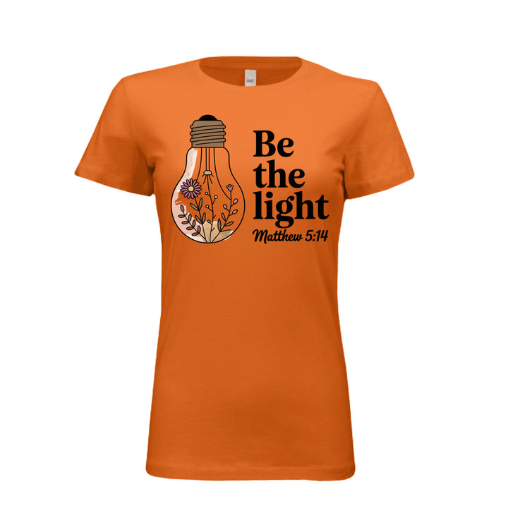 Women's fitted tee in orange with a floral light bulb graphic and the words “Be the light – Matthew 5:14” in bold and script fonts.
