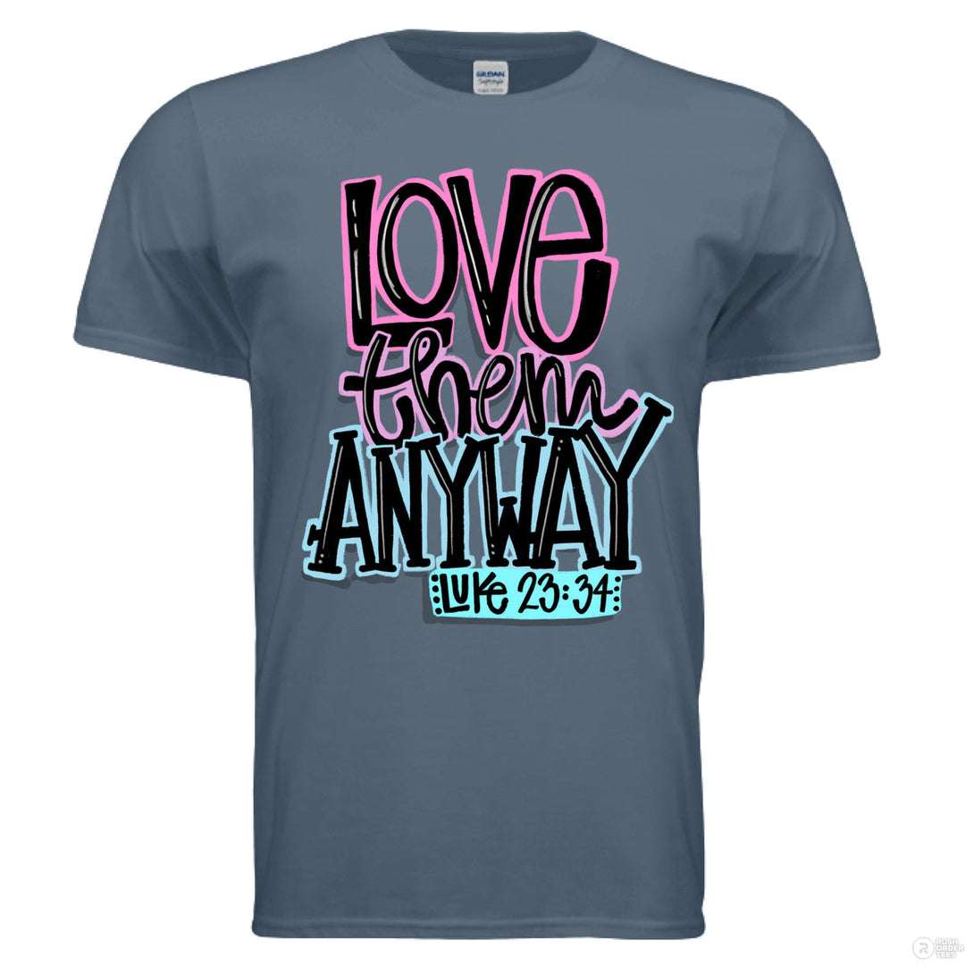 Indigo blue Christian tee with bold lettering in pink, black, and blue that reads “Love them anyway” with scripture reference Luke 23:34
