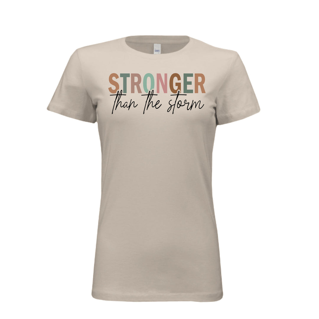 Women's fitted tee in soft cream with bold multi-color “STRONGER” and black script “than the storm” across the chest.
