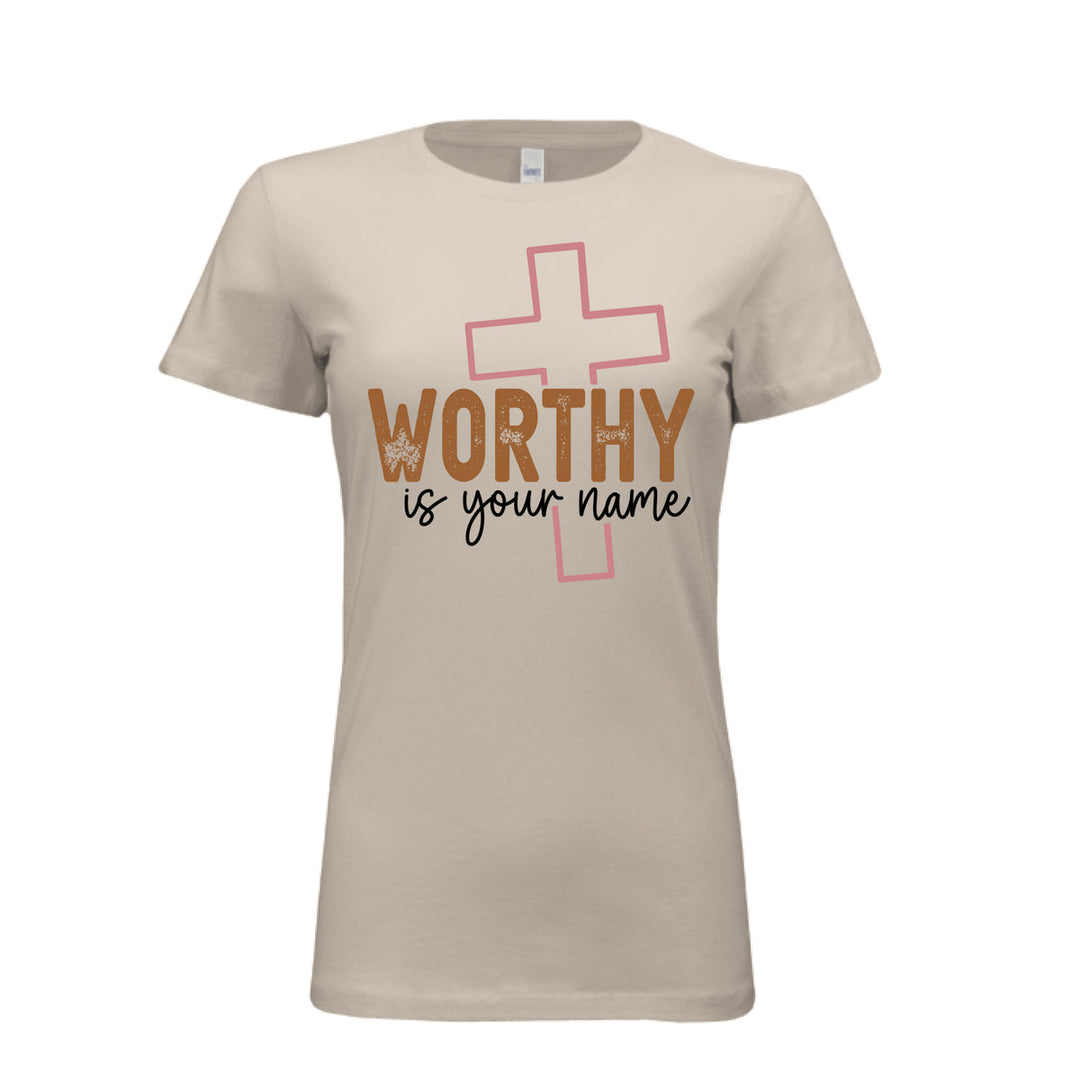 Women’s fitted tee in soft cream with “Worthy is Your Name” text in brown and black, layered over a pink outlined cross
